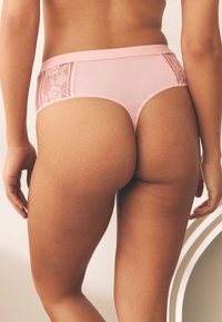 Sous-vêtement rose avec panneaux latéraux en dentelle, finition en tissu lisse, taille mi-haute et coupe sans couture pour un confort et un ajustement optimal.