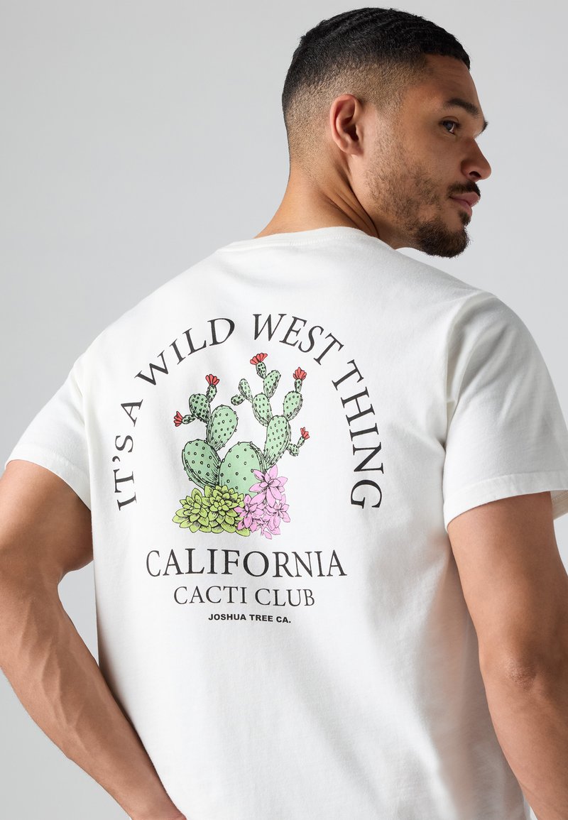 Camiseta de algodón blanca con un gráfico colorido de un cactus en la parte posterior, con el texto "Es cosa del Lejano Oeste" y "Club de Cactus de California."
