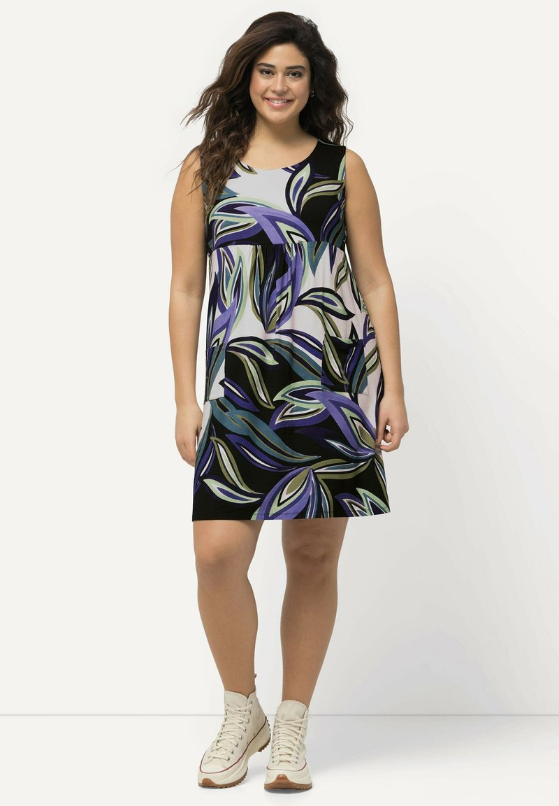 Vestido sin mangas con estampado floral en púrpura, verde y negro; de longitud hasta la rodilla con un cuello redondo. Se lleva con botas de tobillo beiges.