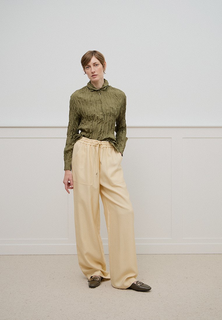 Chemise froissée vert olive avec col, associée à un pantalon large beige clair à taille coulissante et poche avant.