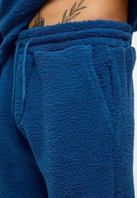 Blauwe fleece joggers met een gestructureerd oppervlak, voorzien van een drawstring tailleband en zijvakken. De stof is zacht en pluche.
