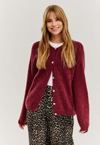Burgundská pletená cardigan s dlhými rukávmi, okrúhlym výstrihom a zapínaním na gombíky, kombinovaná s nohavicami s leopardím vzorom. Mäkka textúra a voľný strih.