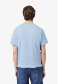Lichtblauwe T-shirt met korte mouwen en ronde hals. Zachte stof, gladde textuur. Draag het met vervaagde blauwe jeans met kleine achterzakdetails.