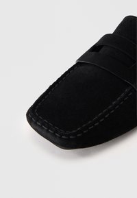 Μαύρες σουέτ λόφερ με τετράγωνη μύτη, διακοσμημένες με ραφές και με λουρί στο επάνω μέρος. Λείο υλικό και μινιμαλιστικός σχεδιασμός.