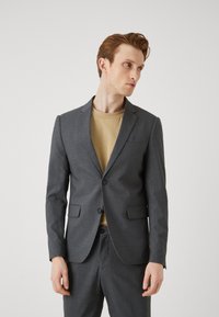 Gray tailored suit jacket with a notched lapel, single-button closure, and two front pockets. Worn over a beige t-shirt. Plain texture.