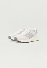 Ljusgrå sneakers med en texturerad ovandel, som har en slät hälkappa och en kraftig vit mellansula. Snörningsdesign med en framträdande logotyp.