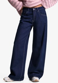 Široke temno jeans hlače z belimi šivi. Imajo klasi�čen pet-pocket dizajn in zaklep s trdnim pasom.