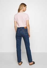 Light pink short-sleeve t-shirt paired with dark blue straight-leg jeans featuring stitching accents and a leather back patch. Casual footwear included.