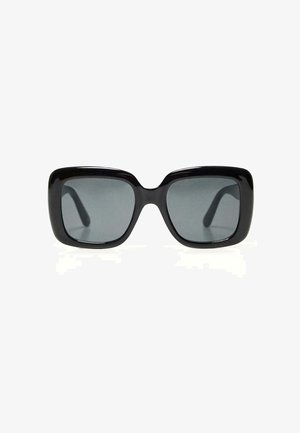 Lunettes de soleil carrées surdimensionnées noires avec des verres teintés foncés et des montures épaisses et brillantes, vues de face sur fond blanc.