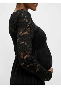 Robe de maternité noire avec des manches longues en dentelle et une taille empire. La dentelle présente des motifs floraux ; la jupe est fluide et lisse.