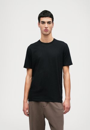 Black cotton t-shirt with a crew neck and short sleeves, featuring a smooth texture. Worn with loose-fitting brown sweatpants.