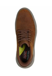 Zapatilla de cuero marrón con puntera redonda, cordones, costuras sutiles y cuello acolchado. Suela de goma gris con detalles de amortiguación en el interior.
