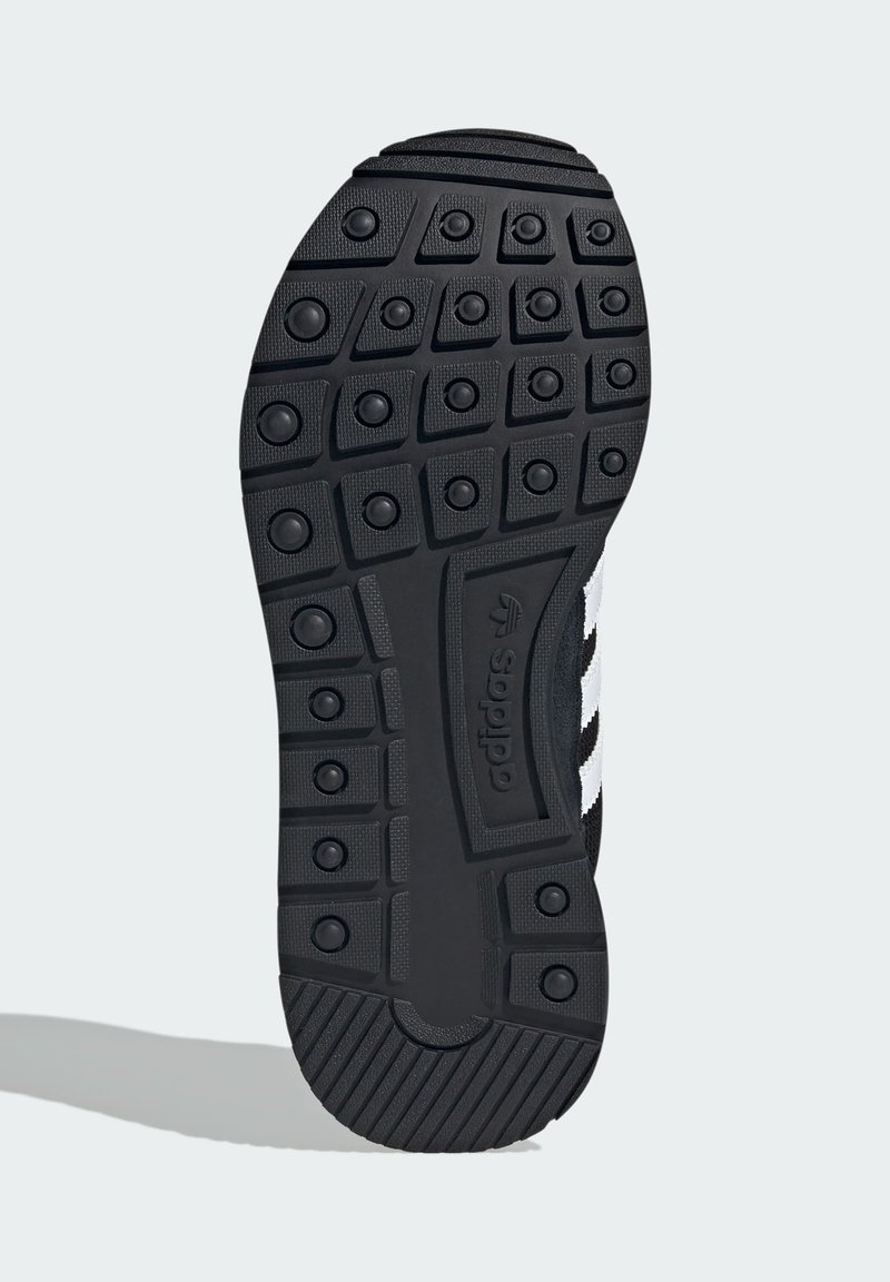 Shoe sole with black rubber tread featuring circular studs, rectangular patterns, Adidas logo, and partial view of black and white upper side.