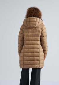 Beige pufferjas met capuchon, voorzien van horizontale gestikte patronen, een gemiddelde lengte en een ritsluiting aan de voorkant. Lange mouwen zijn nauwsluitend.