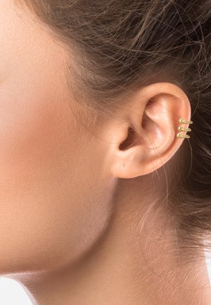 Gros plan d'une oreille latérale avec trois petites boucles d'oreilles manchettes en or sur la partie supérieure de l'oreille et des cheveux châtain clair tirés en arrière.