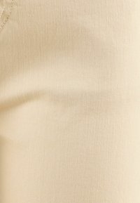 Tissu sergé beige avec une texture de tissage diagonal visible et une couture au coin supérieur gauche.