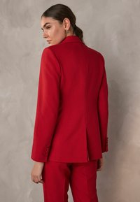 Rød skræddersyet blazer lavet af glat stof, med en spids krave, enkelt bagventil og knapdetaljer på ærmerne.