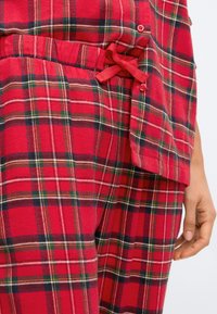 Sada volného oblečení z červeného kostkovaného flanelu, která obsahuje košili s knoflíky a kalhoty se šňůrkou, s akcenty zelené, žluté a černé barvy v designu.