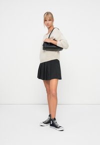 Dzianinowy kremowy sweter i czarna plisowana spódnica. Czarna torebka na ramię o gładkiej fakturze. Czarne sneakersy za kostkę z białą podeszwą i sznurowadłami.