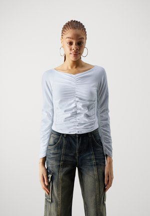 Lichtblauw langmouwen shirt met geplooide details aan de voorkant, gecombineerd met donkere denim wijde cargo-broek met zijzakken.