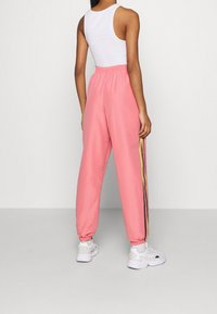 Rosa sweatpants med elastisk midja, utrustad med sidostriper i svart och gult, och avsmalnande mudd. Matcher med vita sneakers.