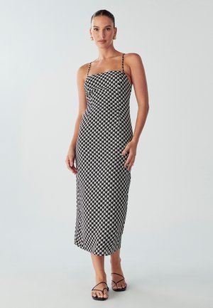 Robe midi à motifs noir et blanc avec des bretelles spaghetti, un bodice ajusté et une jupe droite. Tissu lisse avec un design géométrique.