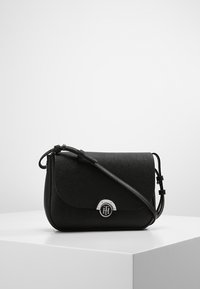 Černá crossbody taška z texturované kůže, s kulatým víkem, stříbrnými doplňky a nastavitelným popruhem pro všestranné nošení.