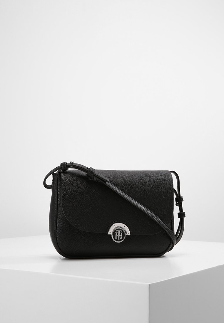 Černá crossbody taška z texturované kůže, s kulatým víkem, stříbrnými doplňky a nastavitelným popruhem pro všestranné nošení.