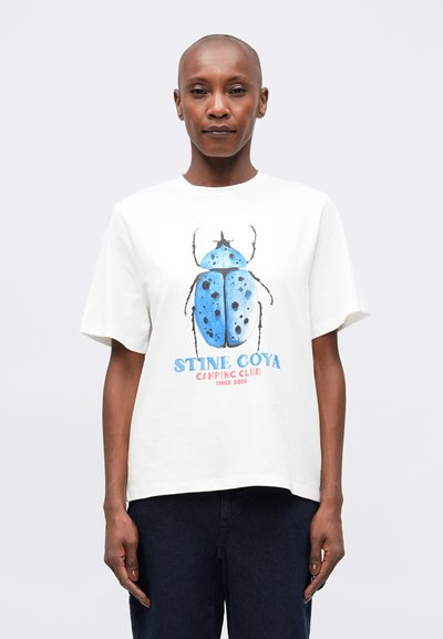 T-shirt en coton blanc avec un grand graphique de scarabée bleu avec des taches noires, présenté avec des manches courtes et une coupe décontractée. Texte "Stine Goya" inclus.