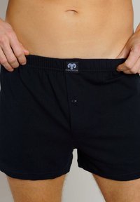 Boxers de algodón negro con una cinturilla suave y elástica, que cuentan con un cierre frontal de botón y una pequeña etiqueta con el logo. Textura suave y corte clásico.