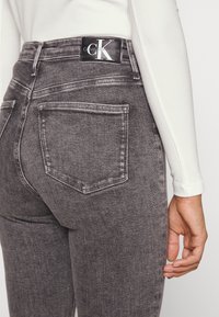 Šedé džínové kalhoty s vysokým pasem, obsahující dvě zadní kapsy alogo Calvin Klein na pasu. Materiál má hladkou strukturu.