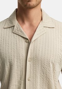 Lichtbeige button-up overhemd met een textuur en geribbelde ontwerp. Bevat een puntige kraag en gladde, lichtglanzende knopen.