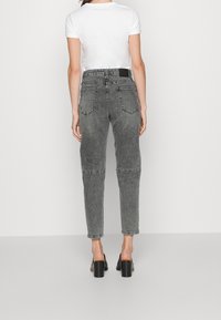 Person som bär högmidjade, gråtvättade jeans med bakfickor, vit kortärmad topp och svarta klackskor, stående vänd bort.