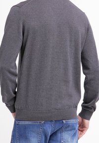 Szary sweter dziany z prążkowanym dołem i mankietami, o gładkiej fakturze i klasycznym kroju, zestawiony z dżinsami.