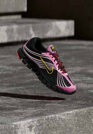 Must roosa spordijalats kollase Nike'i logoga ja punaste nööridega, kujutatud õhus betoonist trepi kohal väljas.