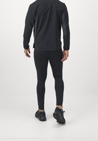 Czarny sportowy top z długim rękawem oraz dopasowane legginsy, wykonane z elastycznego materiału; charakteryzują się bezszwowym wzornictwem i elegancką, minimalistyczną estetyką.
