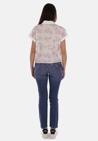 Blusa a maniche corte di colore chiaro con motivo floreale, abbinata a jeans blu scuro e sneakers nere. Dettagli visibili sulla schiena dell'outfit.