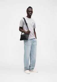 Gray short-sleeve t-shirt with a small yellow logo, light blue baggy jeans, black crossbody bag, and light-colored sneakers.