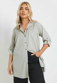 Camicia a righe in verde chiaro e bianco, con taschino sul petto, maniche arrotolate e vestibilità rilassata. Ideale per un abbigliamento casual.