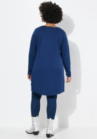 Dunkelblaue Langarm-Tunika mit rundem Halsausschnitt, kombiniert mit dunklen Jeansleggings und silbernen Ankle-Boots, die eine glatte Textur zeigen.