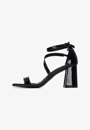 Sandalias de tacón de charol negro con puntera abierta, con dos tiras delanteras y una correa en el tobillo, sobre un tacón grueso.