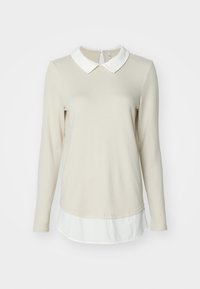 Beige langwerpige top met een witte button-down kraag en zoomdetail. Zachte textuur en rechte silhoutte, minimalistisch ontwerp zonder patronen.