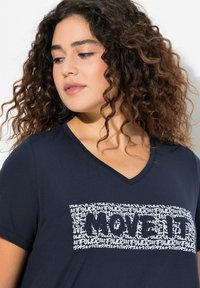 Marinebl�å V-hals t-shirt lavet af blødt stof med et hvidt grafisk design, der har gentagne tekster og fremhæver ordet "MOVE IT" med fede bogstaver.