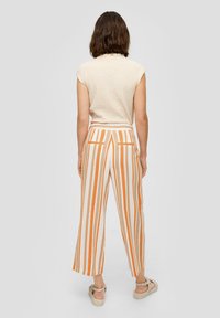 Romantisch crème gebreid topje met korte mouwen, gecombineerd met hoogwaist wijde broek met verticale strepen in oranje en beige en achterzakken.