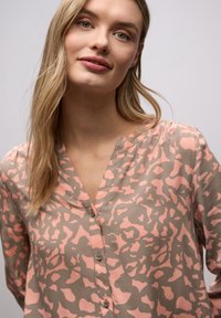 Blouse boutonnée en beige clair avec motif abstrait pêche, présentant un col en V et des manches longues. Tissu lisse avec une coupe décontractée.
