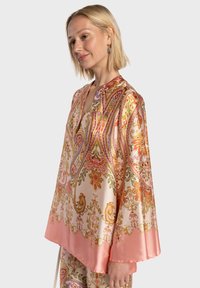 Blouse en soie avec des motifs cachemire et floraux vibrants dans des couleurs pastel. Caractérisée par un col en V et des manches larges avec un ourlet rose uni.