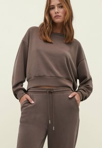 Bruine cropped sweatshirt met lange mouwen en een relaxte pasvorm, gecombineerd met bijpassende joggers met een elastische tailleband en zijzakken.