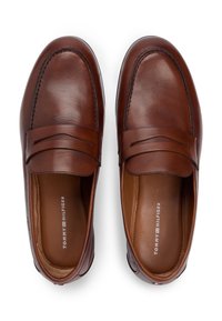 Καφέ δερμάτινα μοκασίνια με ραφές, επίπεδη σόλα και διακοσμητικό λουράκι στο πάνω μέρος. Η επένδυση έχει λογότυπο της μάρκας.