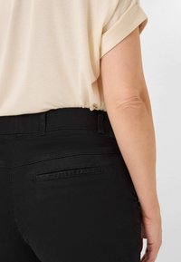 Zwarte denim jeans met een strakke uitstraling, voorzien van een soepele tailleband en subtiele details op de achterkant van de zakken, gecombineerd met een crèmekleurig topje.