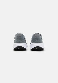 Baskets de sport grises avec une tige texturée, une semelle intermédiaire blanche rembourrée et une semelle extérieure noire. Présente un logo discret et un design globalement épuré.